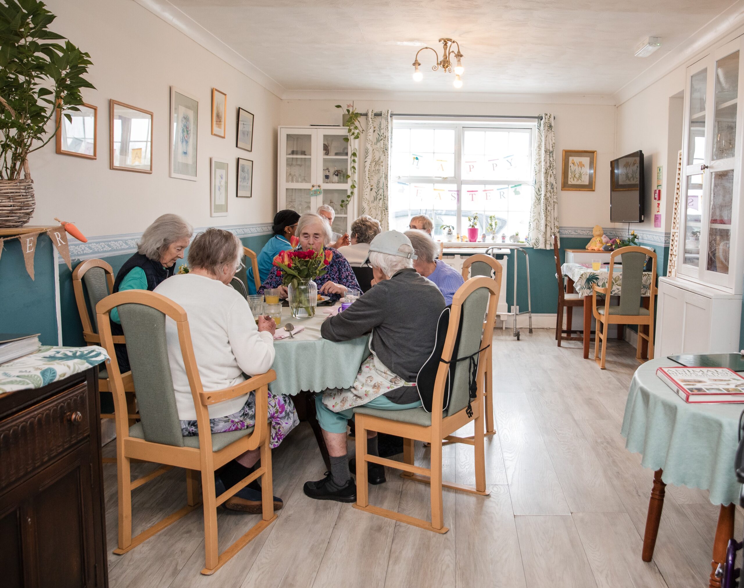 Residents gathered around tables in the bright dining room at Woodfalls Care Home engaging in care home activities